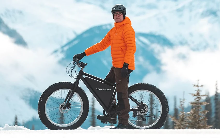 man in orange jacket riding a black sondors electric bicycle